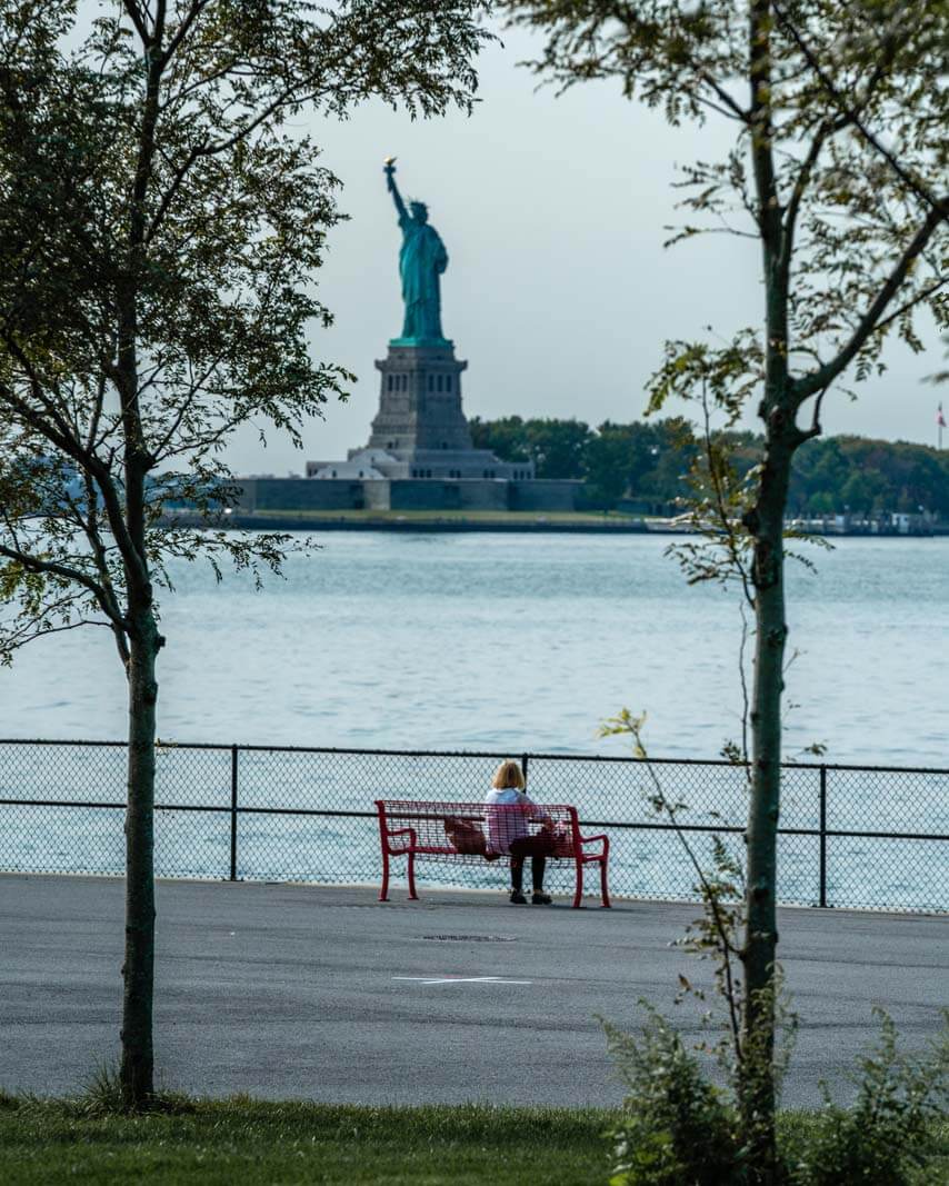 lady on a bench at Governors Island looking at the Statue of Liberty