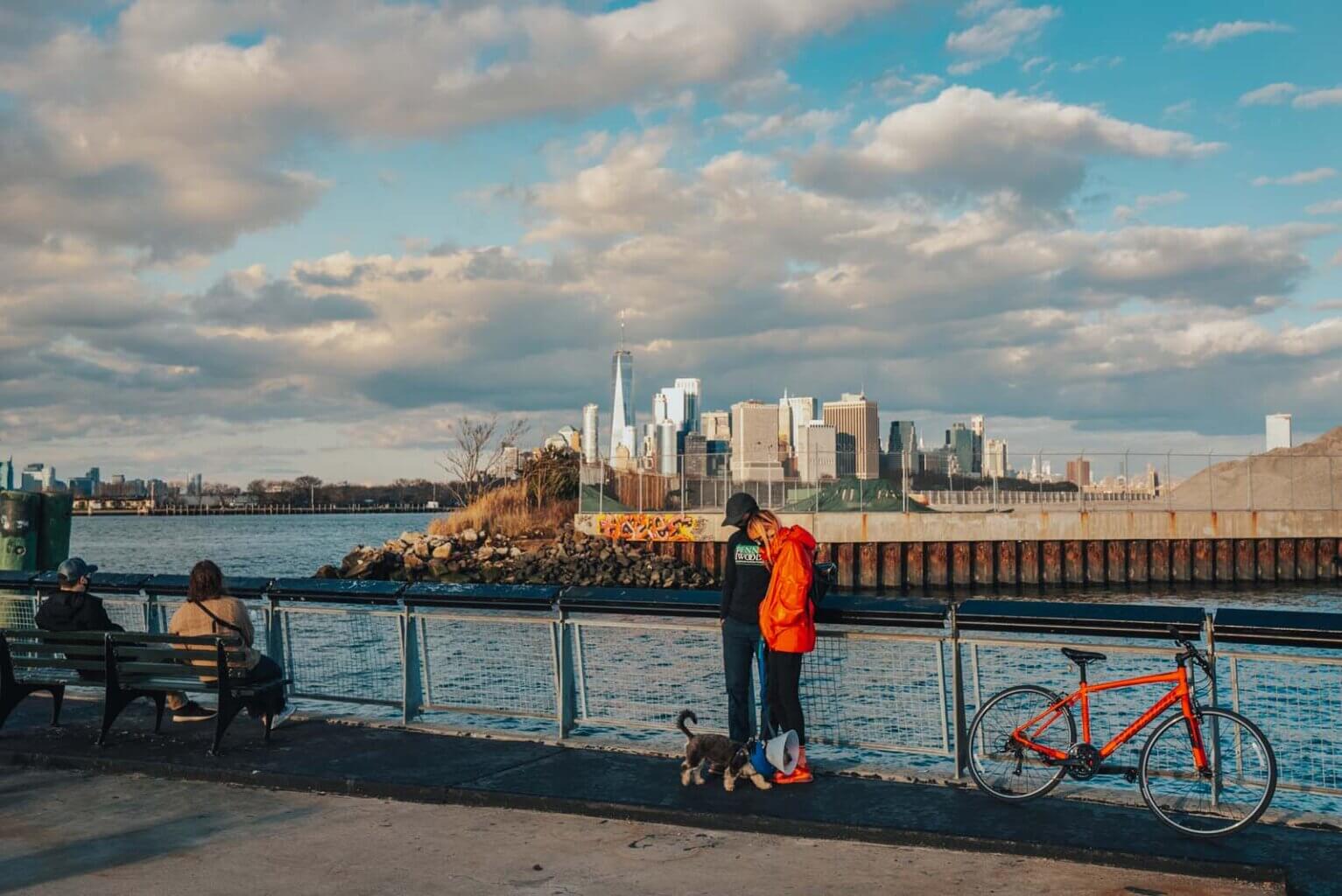 People Standing on the Pier at Louis Valentino Park with a Bench and Manhattan View