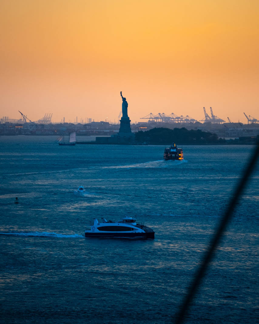 sunset view of the statue of liberty from the brooklyn bridge