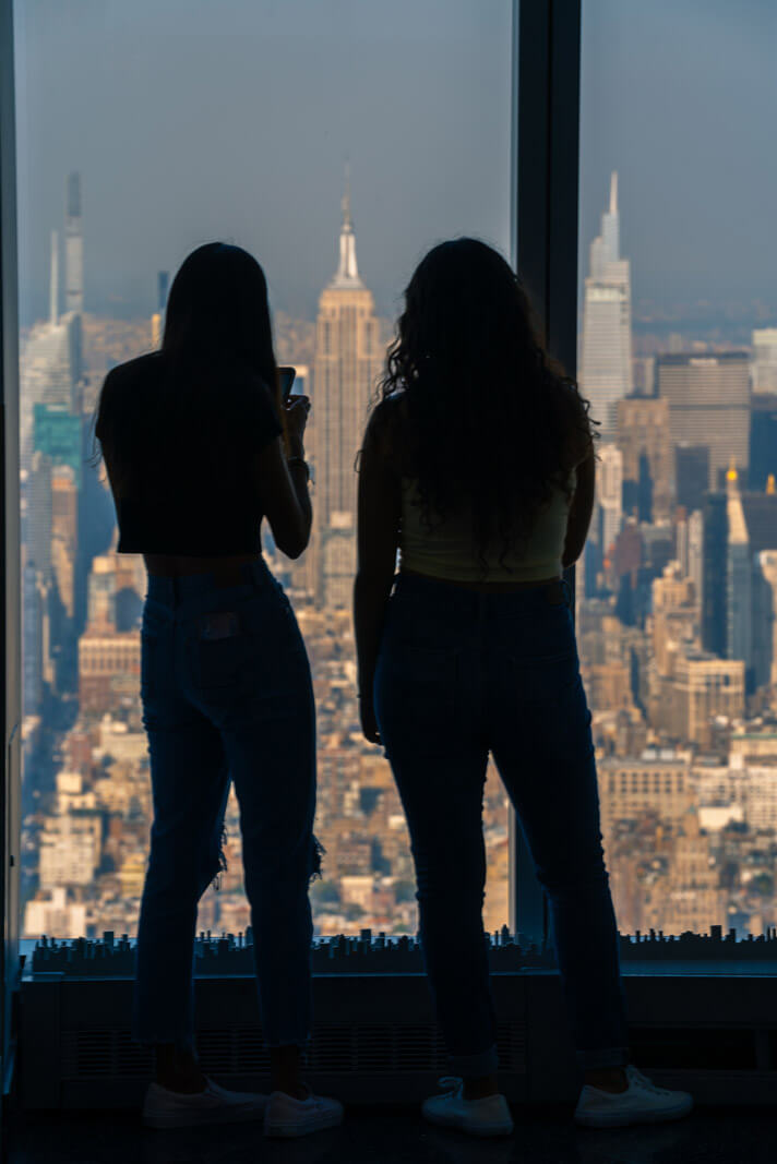 silhouettes of people enjoying the view of the empire state building and nyc skyline from the freedom tower observatory at one world trade center