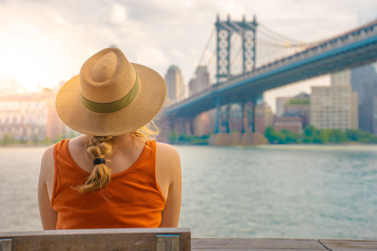 woman-sitting-on-a-bench-in-Brooklyn-looking-at-the-Manhattan-Bridge-in-NYC